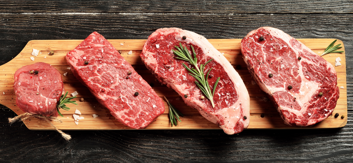 3 rohe Steaks mit Gewürzen auf einem Holzbrett angerichtet